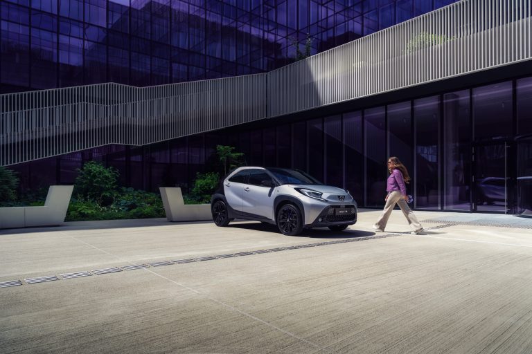 Weißer E-Crossover vor einem modernen Bürogebäude mit Glasfassade.