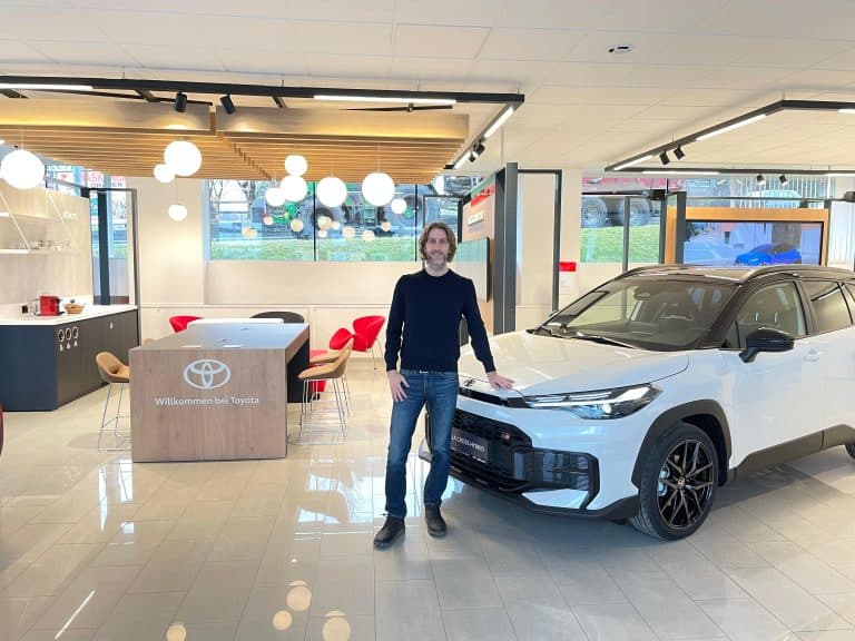 Mann steht neben einem weißen Toyota im Autohaus.